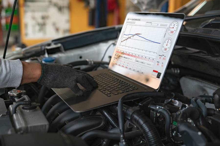 offener Laptop mit Diagrammen auf offener Motorhaube eines Autos