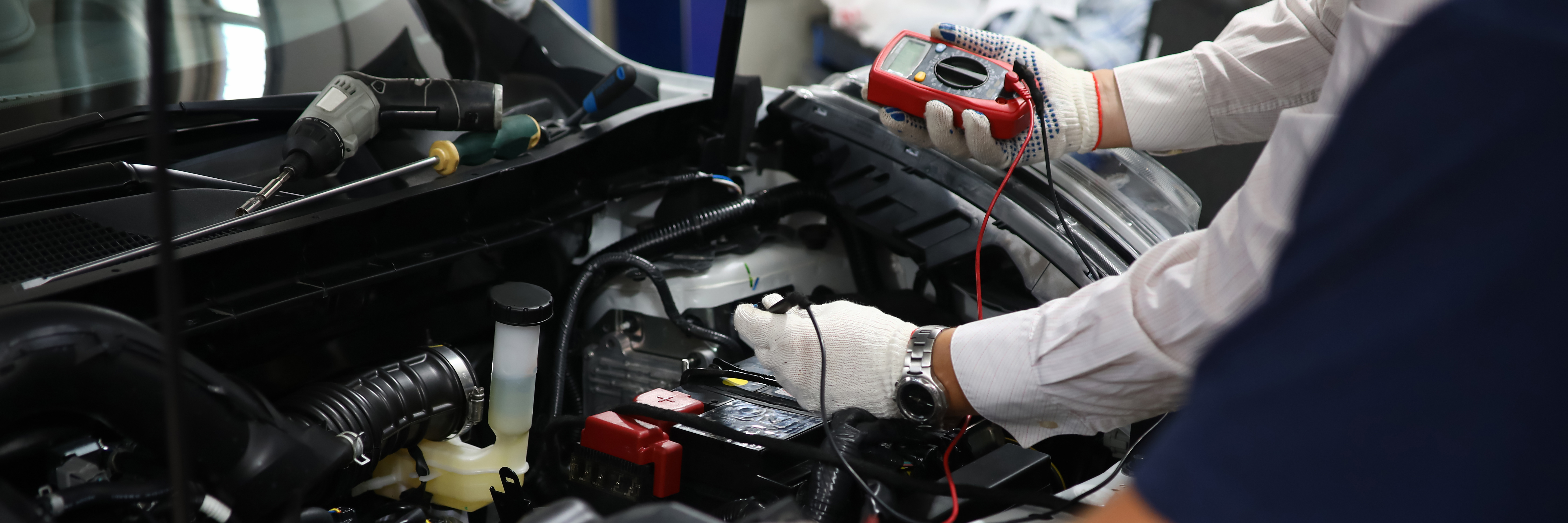 Person mit Handschuhen repariert Autoteil unter der Motorhaube